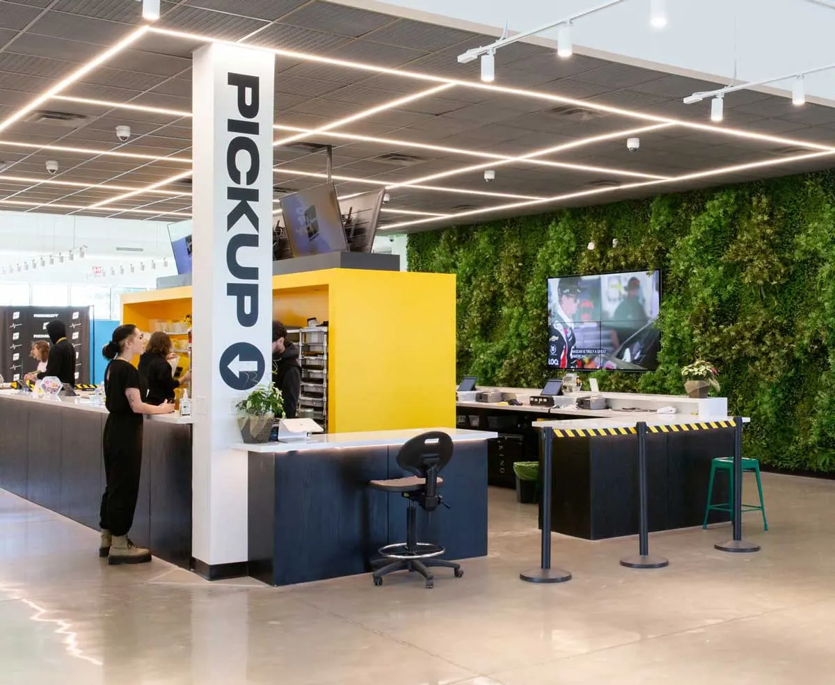 Bright cannabis dispensary interior with pickup counter and green plant wall